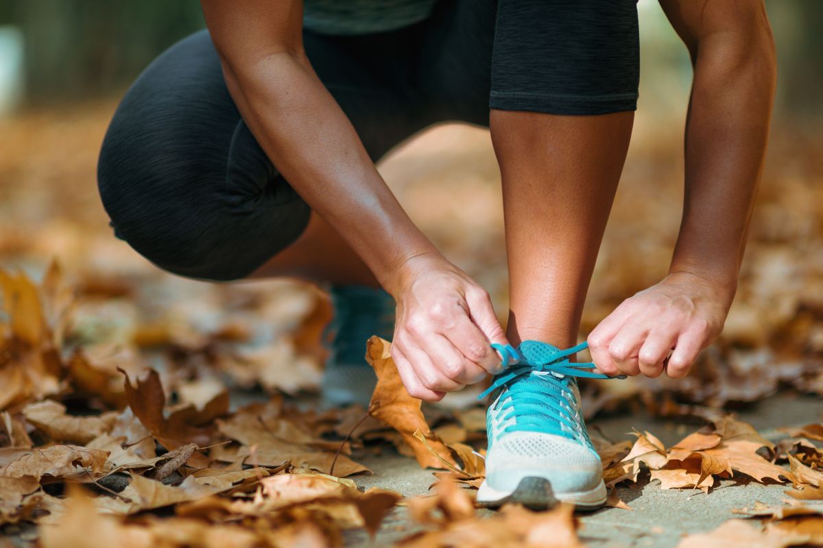 up-close image of a woman tying her shoe among fall leaves