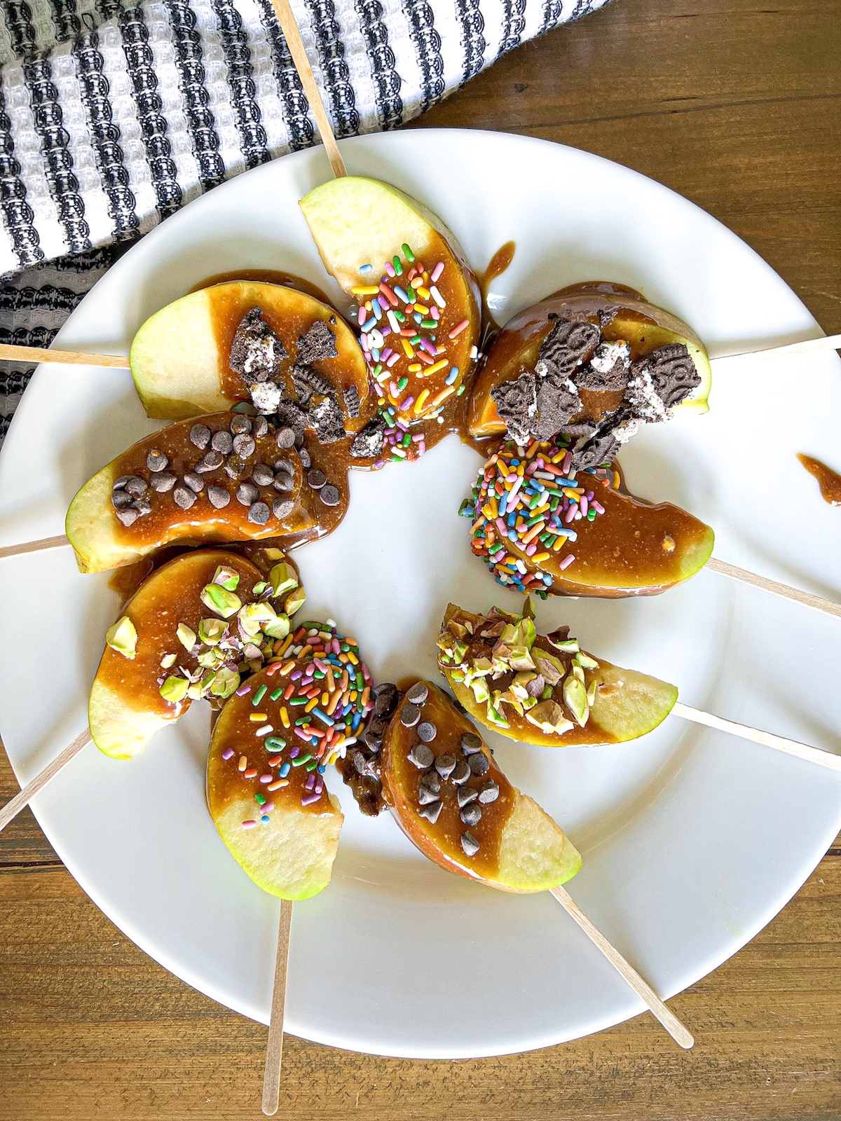 Caramel apple slices with various toppings arranged on a white plate