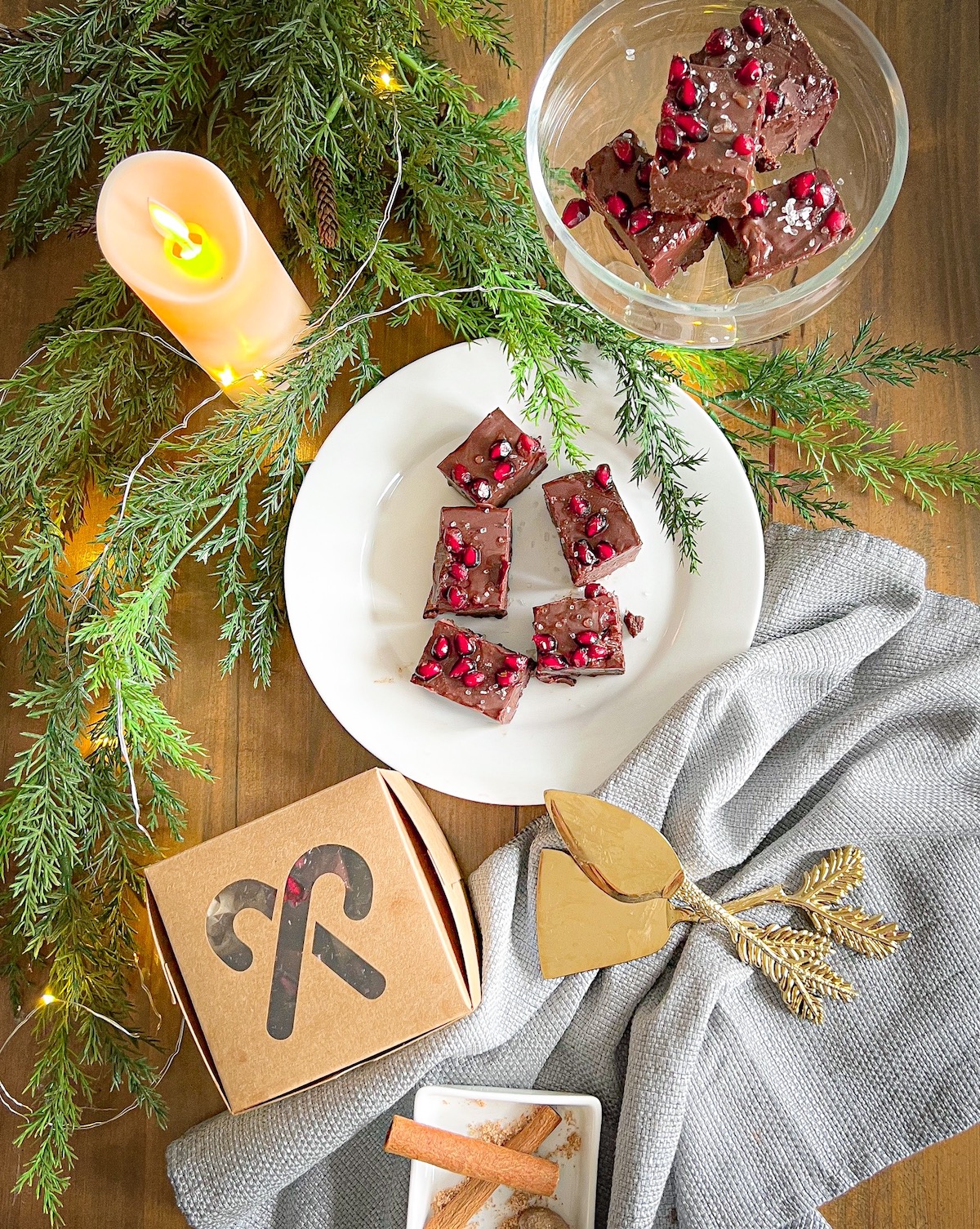 spiced fudge squares in a white plate, on a glass pedestal, and in a holiday treat box with Christmas greenery and lit candle
