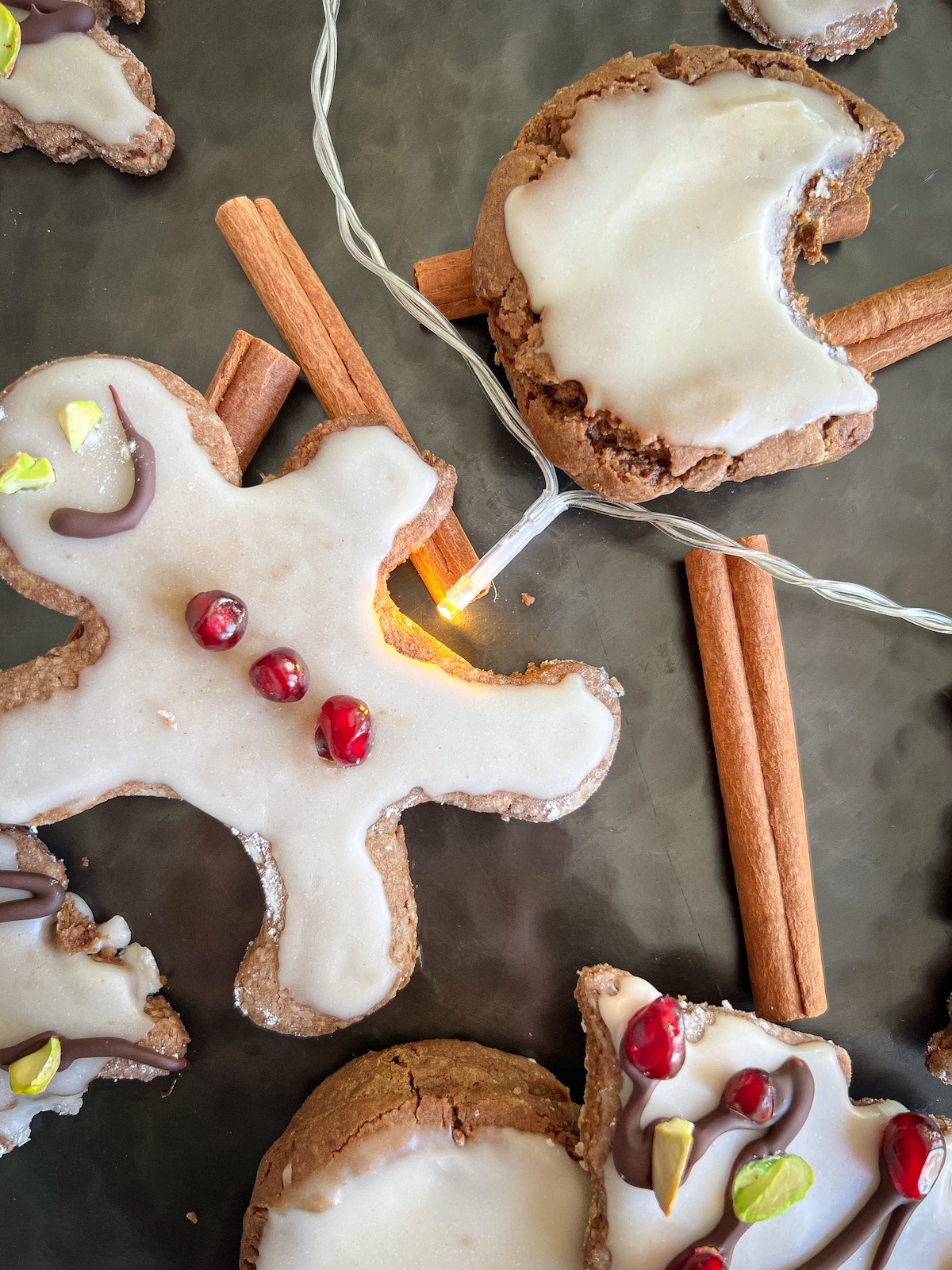 assorted gingerbread cookies on a tray with cinnamon sticks and string lights