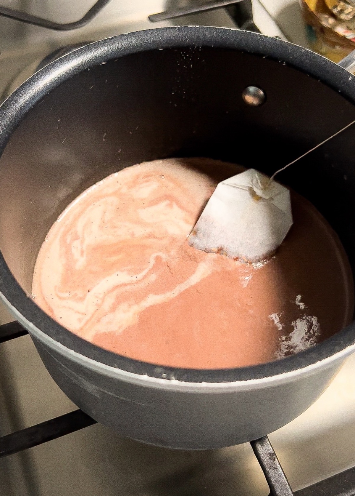 a tea bag steeping inside a small sauce pot of hot cocoa 