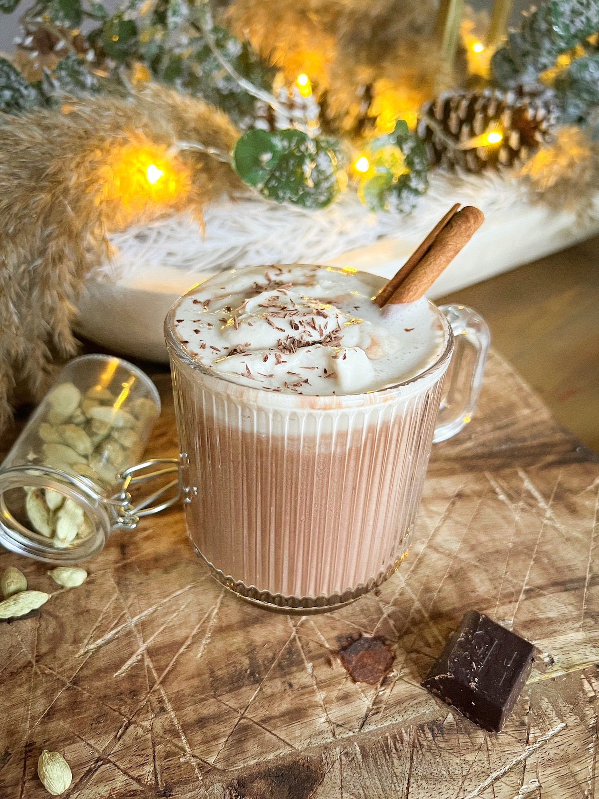 vanilla cardamom hot cocoa in a glass mug with a dollop of coconut whipped cream, chocolate shavings, and cinnamon stick