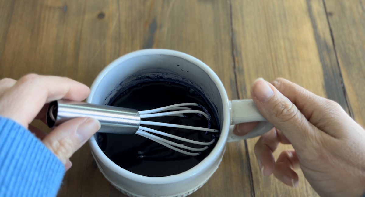 whisking the butterfly pea powder with hot water in a mug